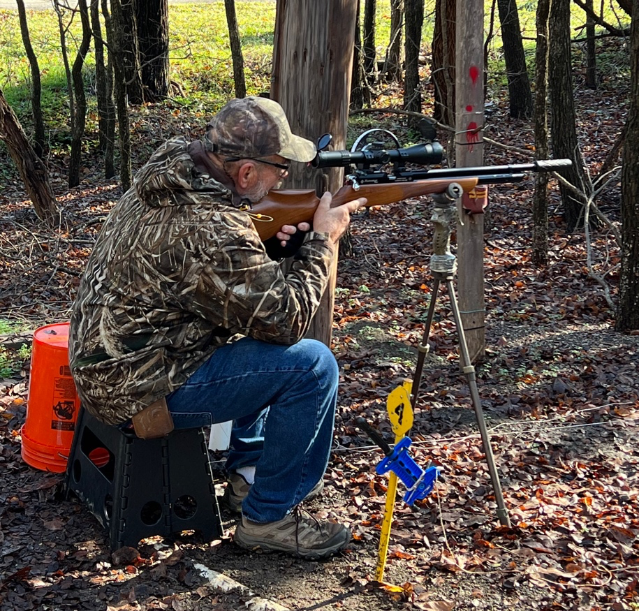 A person sitting on a chair aiming a rifle  Description automatically generated